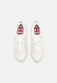 Sneaker con tomaia in pelle bianca e crema, punta arrotondata, chiusura con lacci e marchio "HUGO" in rosso sulla soletta. Dettagli testurizzati presenti.