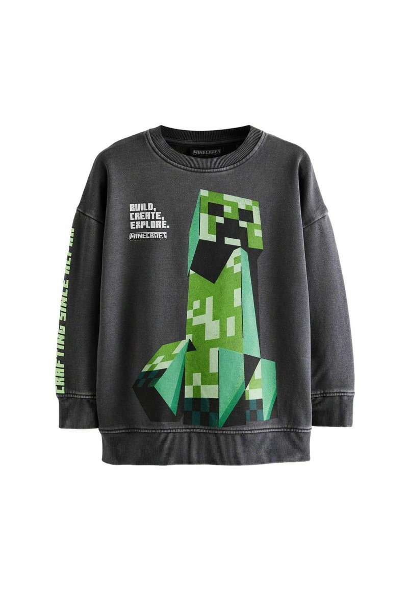 Sweatshirt gris foncé avec un grand graphisme de Creeper pixelisé de Minecraft sur le devant. Le texte indique "CONSTRUIRE, CRÉER, EXPLORER."