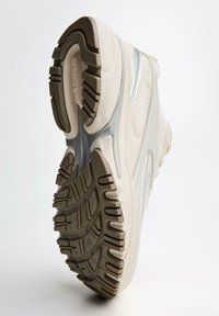 Tenisky s textúrovaným svetlým béžovým zvrškom, lesklými striebornými akcentmi a gumovou podrážkou s hlbokými drážkami a rýhami pre lepšiu priľnavosť.