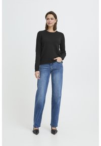 Haut noir à col rond à manches longues associé à un jean droit bleu clair. Le mannequin porte des ballerines noires pointues. Texture de tissu simple, sans motifs.