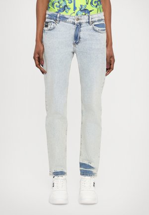 Light blue denim jeans with a straight fit, featuring faded areas, five pockets, and a slightly distressed hem. Worn with white sneakers.