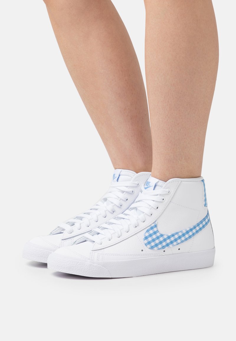 Bele visoke športne copate z teksturiranim finišem, ki imajo Nike swoosh v modrem karirastem vzoru in svetlo modre poudarke na peti.