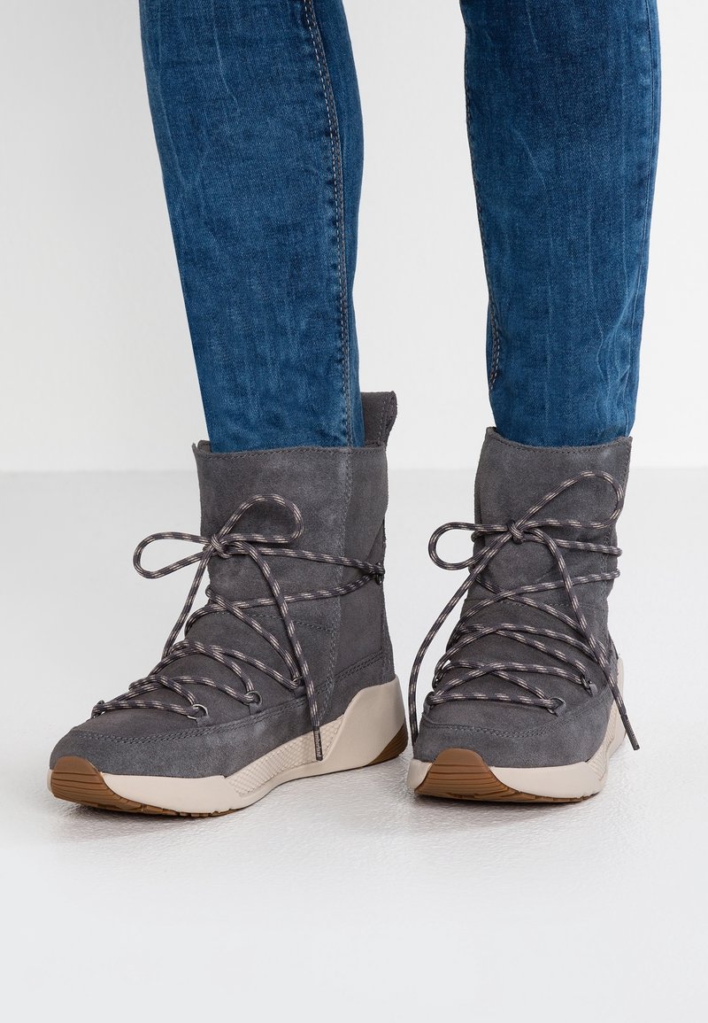 Bottines en daim gris avec un bout arrondi, une semelle beige contrastante et des lacets à motif. Le dessus possède un design avec un renfort pour un soutien supplémentaire.