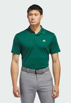 Polo de color verde oscuro con mangas cortas y cuello; presenta un logotipo blanco bordado en el lado izquierdo del pecho; combinado con pantalones grises claros.