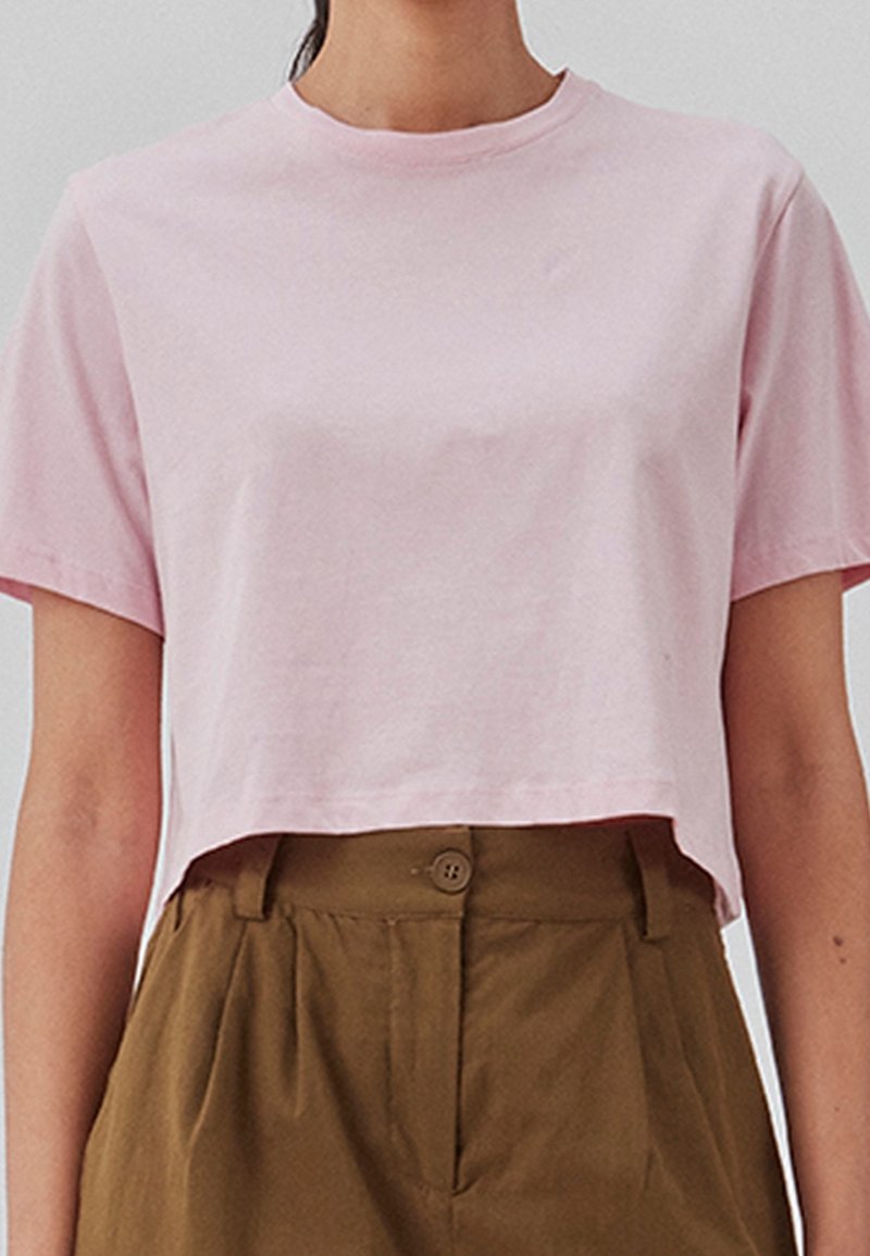 Afklippet, kortærmet t-shirt lavet af lyserød bomuld. Har en rund halsudskæring og en afslappet pasform, parret med højtaljede brune bukser.