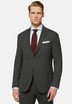 Grau maßgeschneiderte Sakko mit Revers, zwei Knöpfen und Klapptaschen. Dazu ein hellblaues Hemd und eine bordeauxfarbene Krawatte mit einer Einstecktuch.