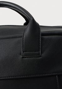 Čierna kožená taška s hladkou textúrou. Má zaoblené rúčky a kontrastné prešívanie. Vrch tašky má štruktúrovaný dizajn s minimálnymi detailmi.