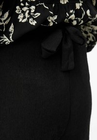 Tela negra texturizada con un top de patrón floral con volantes. Presenta un detalle atado en la cintura, enfatizando una silueta ajustada.