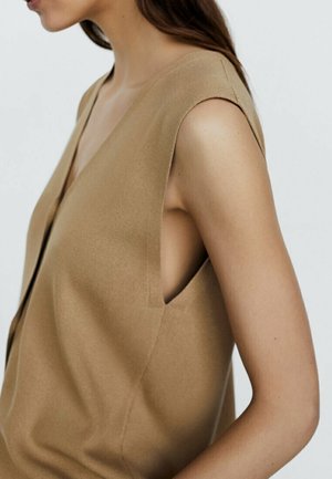 Ärmelloses, hellbeiges Oberteil mit tiefem V-Ausschnitt, weicher Textur und minimalistischer Gestaltung, die ausgeschnittene Seiten umfasst und eine klare Silhouette präsentiert.