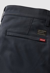 Pantaloni din denim negri cu o textură netedă, având o buzunar în spate, etichetă de marcă din piele și un logo Levi's roșu.
