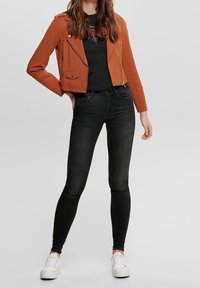 Ochroniowa kurtka motocyklowa z sztucznej skóry na czarnej koszulce z grafiką, połączona z czarnymi obcisłymi dżinsami i białymi trampkami. Proste detale zamka.