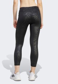 Leggings neri con una speciale stampa animale testurizzata, vita alta e design aderente. Abbinati a scarpe da ginnastica bianche con strisce nere.