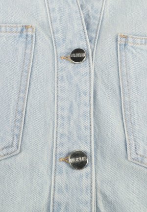 Lichtblauwe denim stof met twee metalen knopen gegraveerd met "NUKUS" en zichtbare stiksels rondom twee rechthoekige zakken.