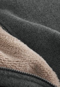Tessuto in pile grigio scuro con un morbido rivestimento interno beige. Presenta una cerniera liscia lungo il bordo, che mette in evidenza una texture a contrasto.