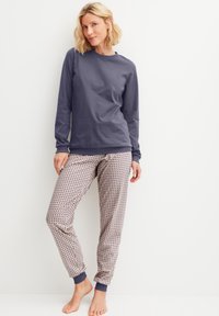 Marineblaues Langarmoberteil kombiniert mit gemusterten Pyjamahosen mit beiger Basis und blauen Akzenten an den Bündchen. Baumwollmaterial, lockere Passform.
