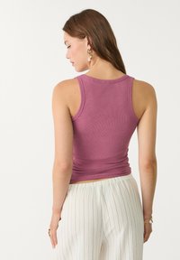 Taillierte, gerippte rosa Tanktop mit rundem Ausschnitt. Trägt dazu strukturierte weiße, hochtaillierte Hose. Minimalistisches Design, keine sichtbaren Muster.
