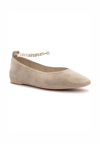 Zapato plano de ante beige con punta afilada, que cuenta con una correa para el tobillo de cadena dorada y una suela de goma plana. Textura suave en todo el zapato.