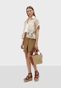 Lace-knit cream blouse, white shirt, tan shorts, brown wedge sandals, and a woven tote bag with leather accents.