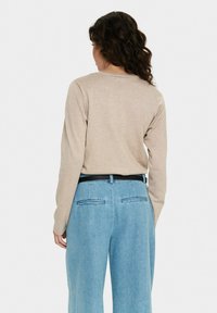 Gaišbeigas krekls ar garām piedurknēm un apaļu kakla izgriezumu, apvienots ar gaiši zilām augstās jostasvietas džinsu biksēm, kurām ir melna josta un divas aizmugures kabatas.