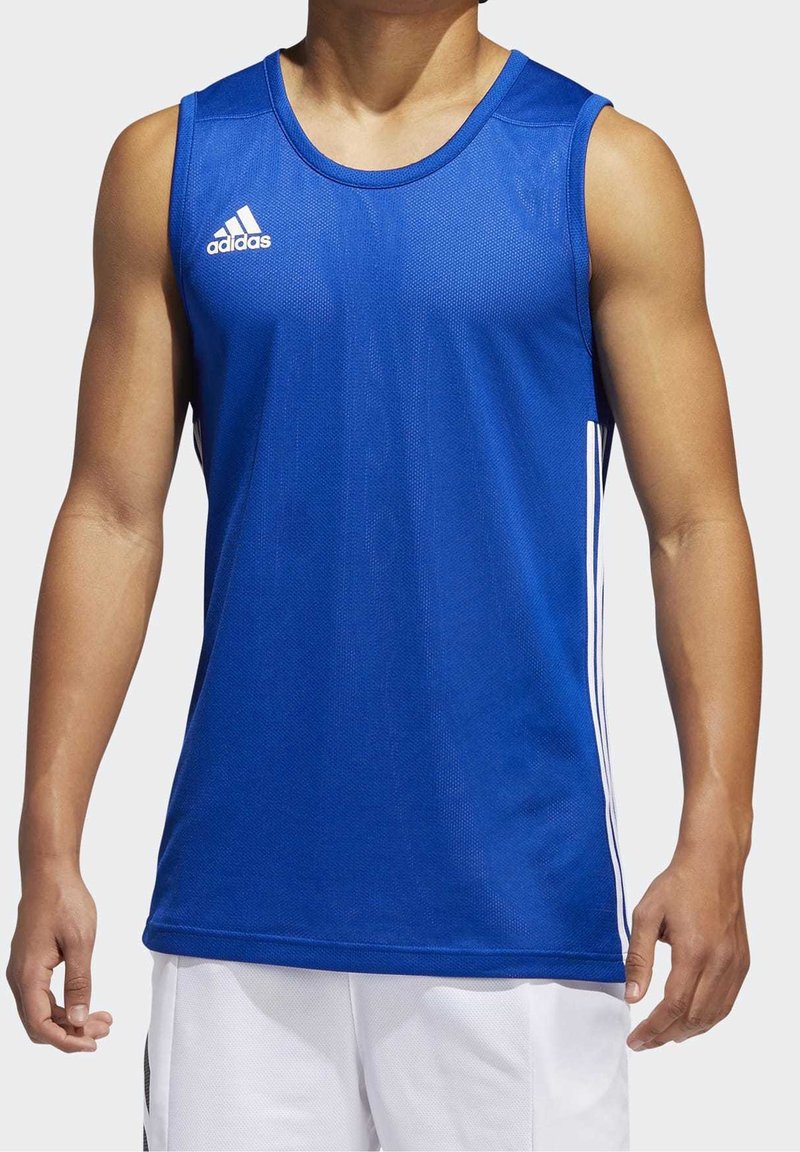 En man som bär en ärmlös blå Adidas sporttröja med vita ränder på sidorna och vita shorts mot en enhetlig bakgrund.