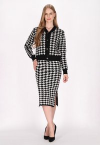 Černobílý houndstooth pletený kardigan s knoflíky, spárovaný s odpovídající tužkovou sukní s bočními rozparky a texturovanou tkaninou.