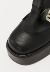 Must musta kingad, millel on ümar nina, paks platvormtalda ja külgedel lõikeavad. Sile tekstuur ja minimaalsed aktsendid.