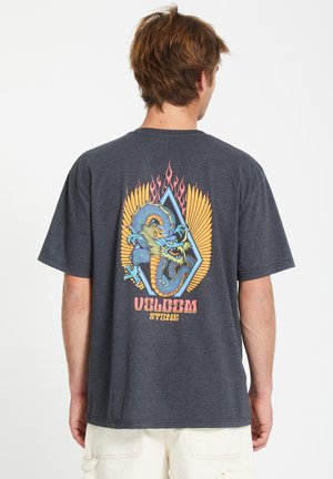 T-shirt a maniche corte grigio scuro con un'illustrazione colorata di un drago, circondata da motivi di ali e fiamme, con il testo "VOLCOM" in basso.