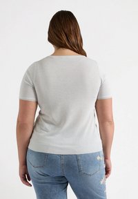 Jasnoszara bluzka z krótkim rękawem, okrągłym dekoltem i ryżowym dołem. W zestawieniu z niebieskimi dżinsami z haftem kwiatowym na tylnej kieszeni.