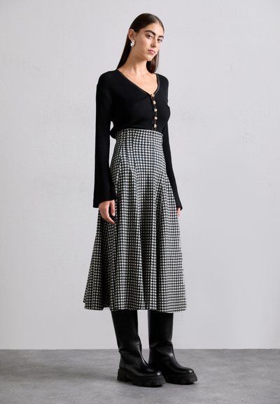 Črn rebrast dolgrokavnik s gumbi, v kombinaciji s krilom do kolen, ki ima črno-belo houndstooth vzorec. Črni gležnjarji.