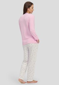 Top de manga larga color rosa claro con cuello redondo, combinado con pantalones crema que presentan un patrón de pequeños corazones morados. Textura de tela suave.