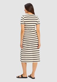 Gestreepte gebreide jurk in crème en zwart met korte mouwen, knie-lengte, textuurstof, en platte zwarte sandalen.