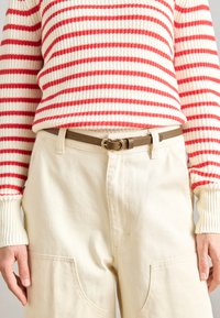 Maglione a righe rosse e bianche in maglia con polsini a costine, abbinato a pantaloni color crema con grandi tasche e una cintura beige con fibbia rotonda.