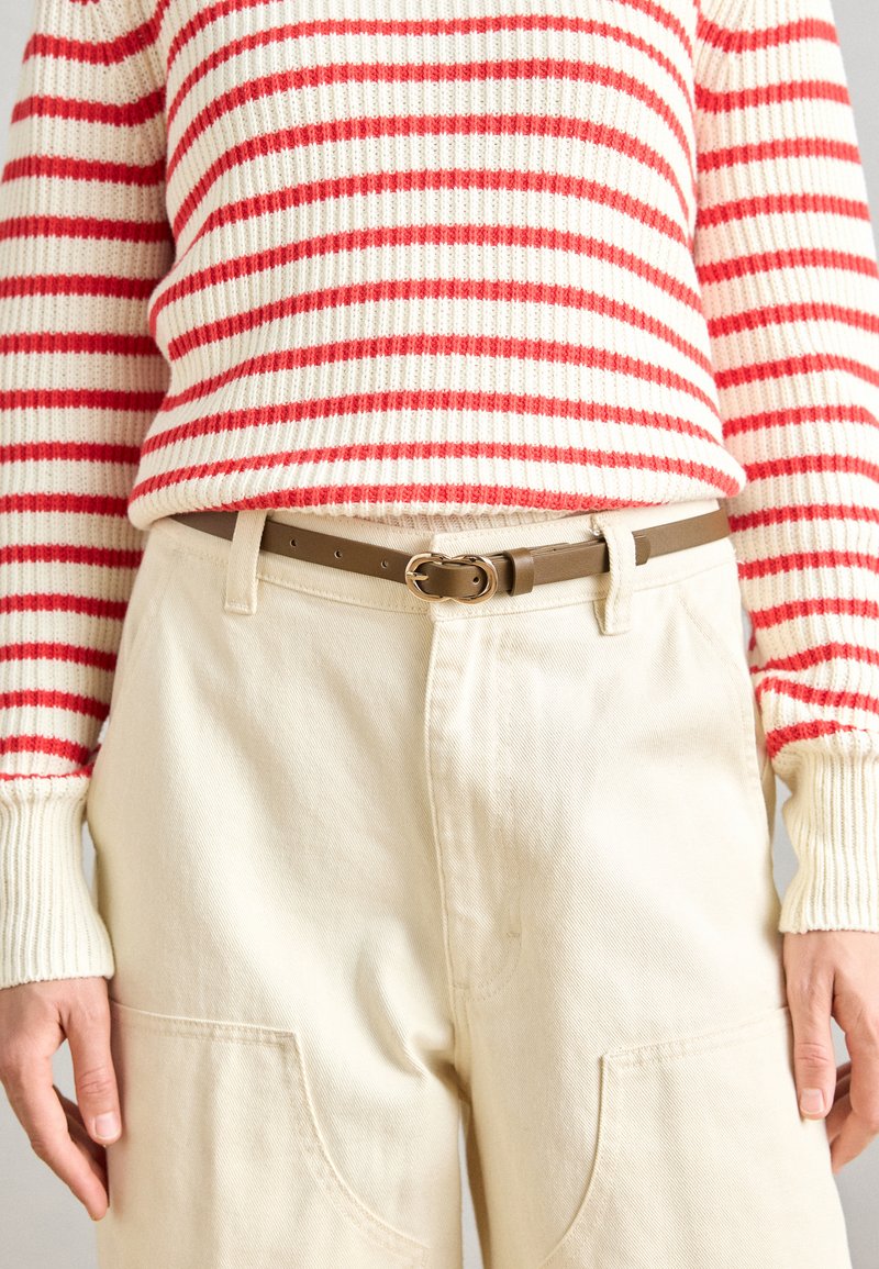 Maglione a righe rosse e bianche in maglia con polsini a costine, abbinato a pantaloni color crema con grandi tasche e una cintura beige con fibbia rotonda.