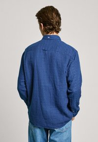 Long-sleeve shirt in navy blue fabric featuring a subtle patterned texture and a button-down collar, with a rounded hem and button details.