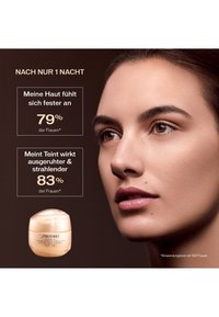 Shiseido Cremedose in milchigem Pfirsichfarbton, runde Form und transparentem Deckel. Modell mit glatter Haut, neutralem Make-up und natürlichem Licht.