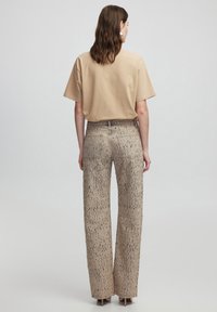 Camiseta de manga corta beige combinada con pantalones beige de pierna ancha con manchas, que presentan una textura sutil y bolsillos traseros.