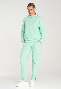 Miętowa bluza z wysokim kołnierzem, połączona z miętowymi spodniami typu tapered z bocznymi kieszeniami i rozcięciami na kostkach. Białe sneakersy.