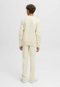 Sweatshirt amarelo claro e calças em coordenação feitas de tecido macio. Corte descontraído com punhos canelados, usado com ténis brancos. Vista traseira.
