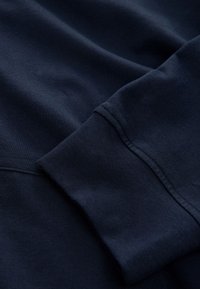 Tissu de sweat-shirt bleu marine foncé avec couture visible au niveau du poignet et texture douce en gros plan.