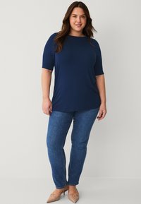Navyblaues kurzärmeliges Oberteil mit lockerer Passform, kombiniert mit dunkelblauen Slim-Fit-Jeans und beigen spitzen Absätzen. Einfaches Design, glatte Textur.