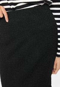 Fustă creion texturată neagră, cu un fit slim, având o talie netedă și un model vertical. Asortată cu un top cu dungi vizibil la mânecă.