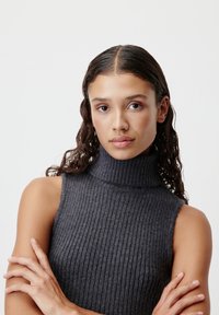 Tumši pelēks, ribotais turtlenecks bez piedurknēm ar augstu kaklu. Mīksta tekstūra ar pieguļošu siluetu, atklājot plecus un rokas.