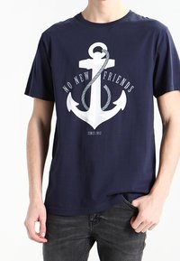 Camiseta azul marino con un gran gráfico de ancla blanca acompañado de una cuerda retorcida, con el texto "NO NUEVOS AMIGOS" arriba y "DESDE 2012" abajo.