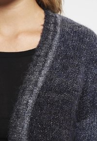 Gebreide cardigan in donkergrijs en marineblauw. Gekenmerkt door een textuur met een zachte stof, een geribde kraag en een open voorkant.