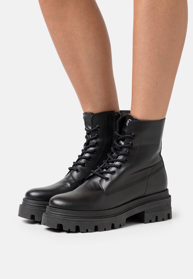 Bottes chelsea en cuir noir avec bouts ronds, laçage à l'avant, fermeture éclair latérale et semelles épaisses texturées. Présente des détails de couture minimalistes.
