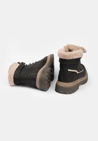 Botas negras hasta el tobillo con un cuello de piel sintética, suela de goma texturizada, parte frontal con cordones y un acabado de cuero suave. Costuras laterales en color beige como acento.