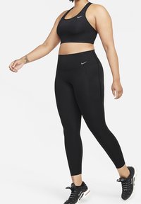 Czarny zestaw sportowy składający się z biustonosza sportowego z plecakiem i spodni legginsowych o wysokim stanie. Oba elementy mają elegancki design z dyskretnym logo Nike.