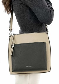 Bolso bandolera de cuero beige y negro con superficie texturizada, un bolsillo frontal con cremallera y una correa ajustable, con detalles de herrajes plateados.