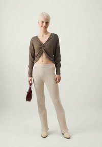 Brown, ribbed, long-sleeve crop top with a front knot, paired with beige ribbed pants and light beige heels; holding a dark red handbag.