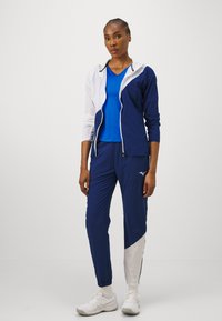 Jūras spēku un baltā sporta jaka ar rāvējslēdzēju, pāris ar zilu topu un tumši ziliem biksēm ar gaiši pelēku akcentu un logotipu. Strukturēta auduma.